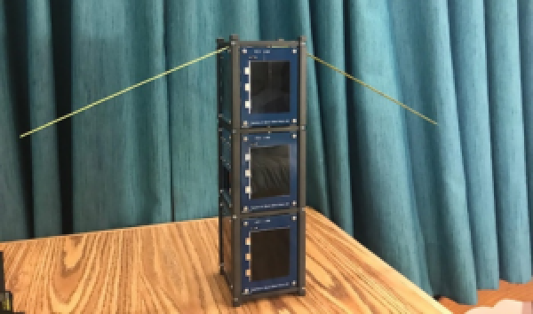 Serenity 3u CubeSat Satellite miniature structure example sitting a wooden table with a green background.
