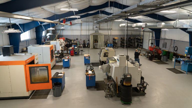 Innovative Machining Services machine shop with various testing rigs on display, with a man walking in the background.