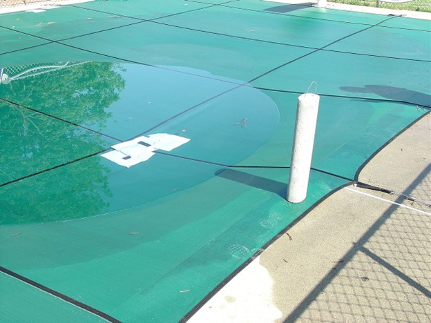green swimming pool cover that has gone through product compression testing covering an inground pool