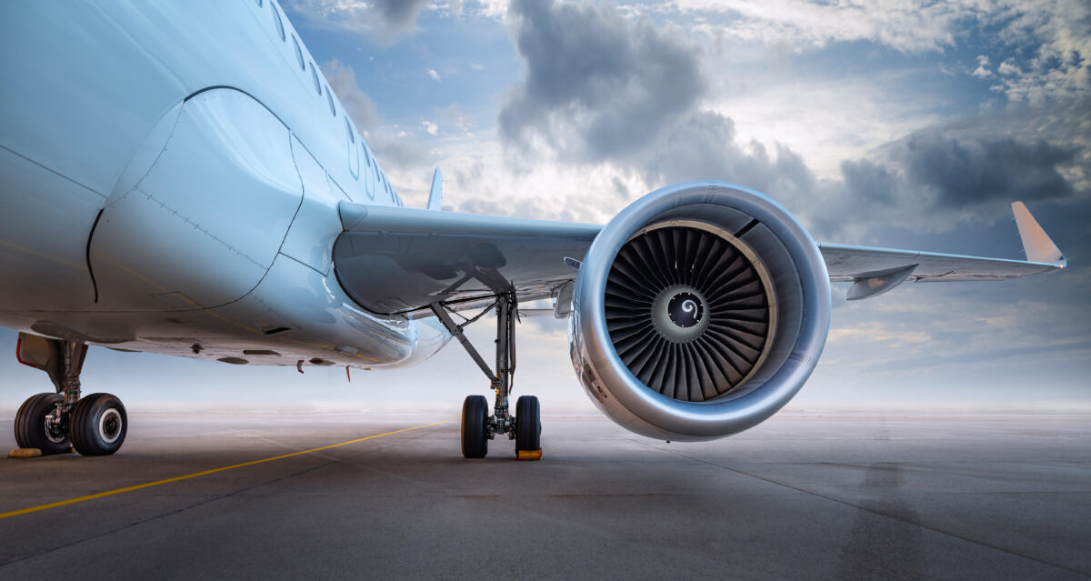 A close-up view of part of a commercial airliner on a runway with the engine turbine facing forward; cloudy sky in the background. 